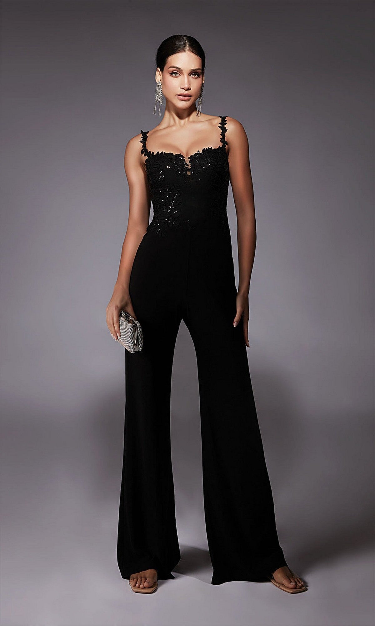Woman wearing the Alyce 70073 Long Formal Jumpsuit in black, featuring a sleeveless design with sequin details, holding a silver clutch against a neutral background.